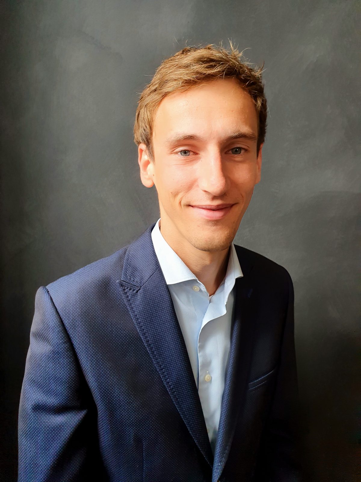 Een jonge man in pak lacht voor een zwarte achtergrond voor Rocket Hypotheken.