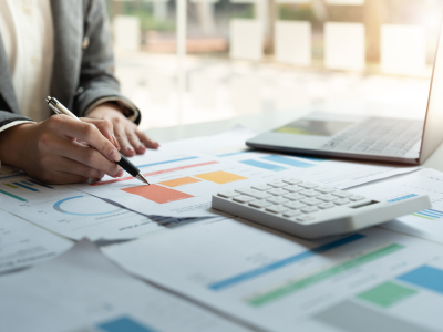 Persoon die grafieken en diagrammen analyseert aan een bureau met een laptop en een rekenmachine.